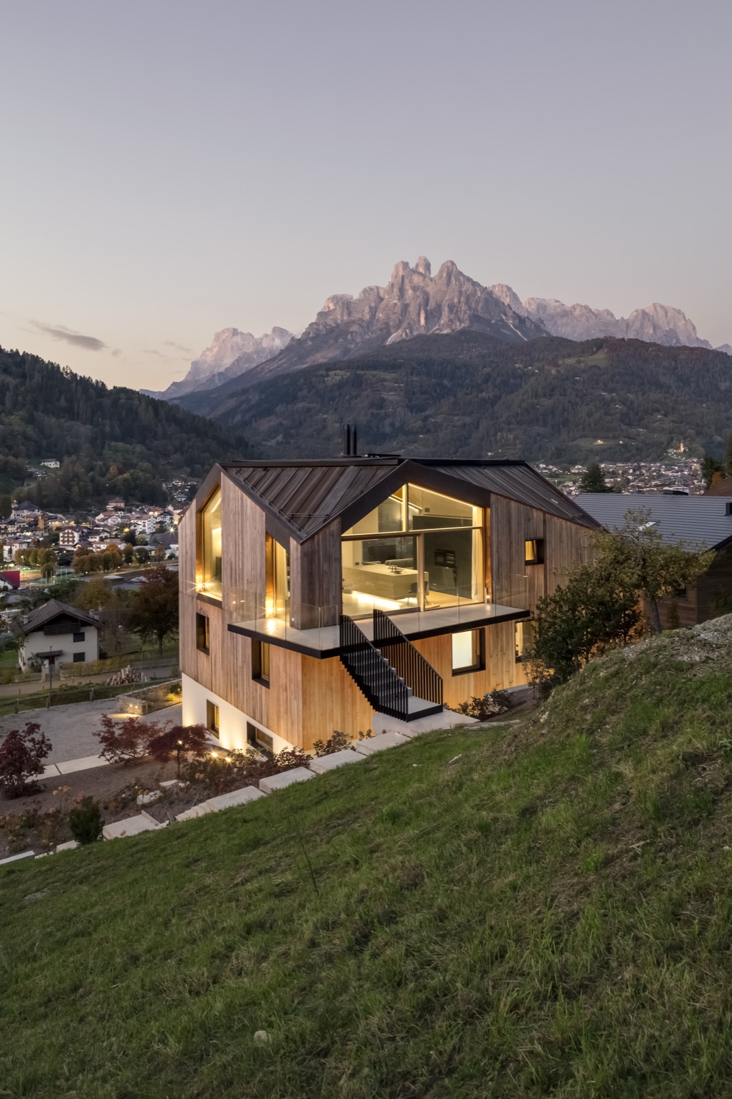L'architettura in legno di Casa LAGO Dolomiti al crepuscolo, con le finestre illuminate affacciate sulle Pale di San Martino
