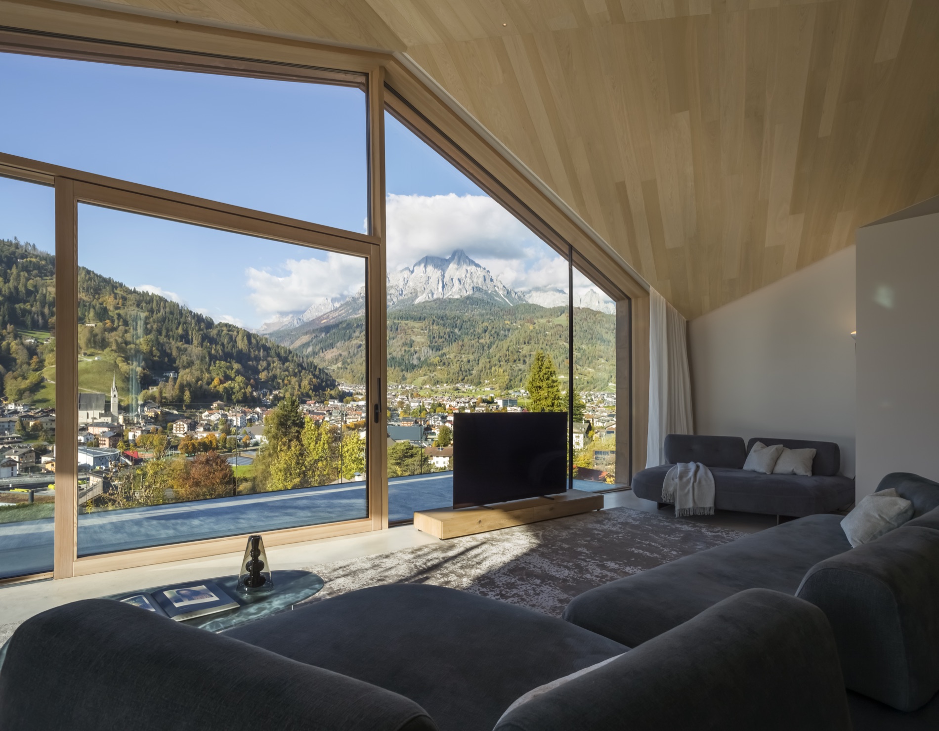 Il soggiorno panoramico di Casa LAGO Dolomiti, con grandi vetrate aperte sul borgo di Primiero e sulle montagne
